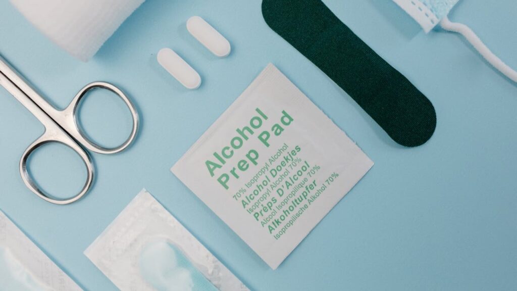 Medische hulpmiddelen voor wondverzorging, waaronder alcoholpads, schaar en pleisters op een blauwe ondergrond