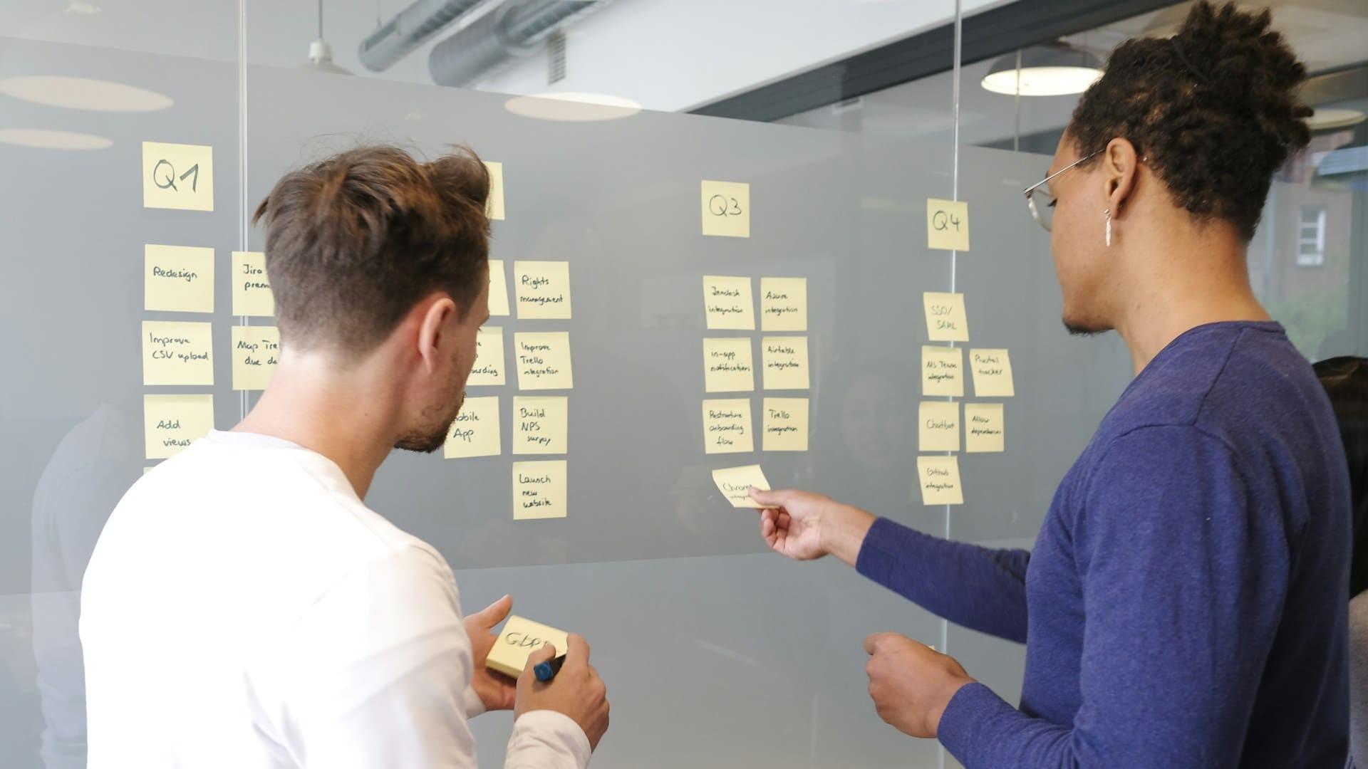 Team dat taken structureren met post-its op een glazen bord tijdens planningsoverleg