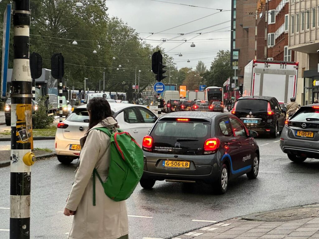 Druk kruispunt met auto’s, tramleidingen en voetganger met groene rugzak in de stad